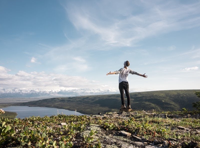 Person with arms outstretched in a T shape on a hill overlooking a lake